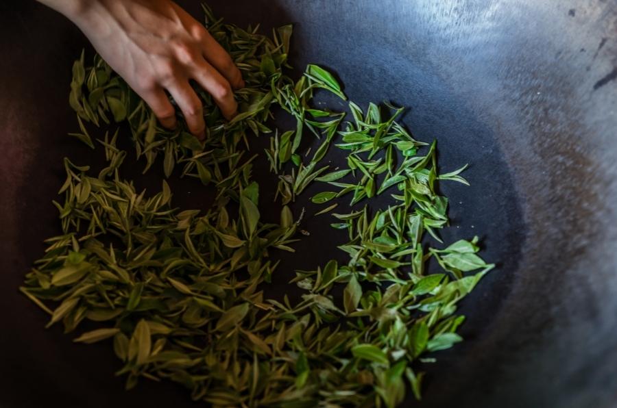 Hand-pressing and tossing tea leaves on a wok.