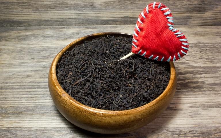 A bowl with loose leaf black tea with a red sewn heart on a stick.