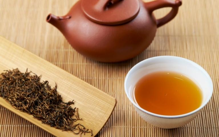 Loose-leaf black tea, a porcelain cup of black tea and a ceramic teapot.