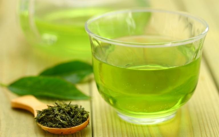 Loose-leaf Japanese green tea on a spoon and it's bright green infusion in a transparent cup.