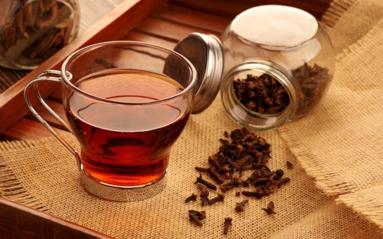 Scattered pieces of clove and a clove infusion in a cup.