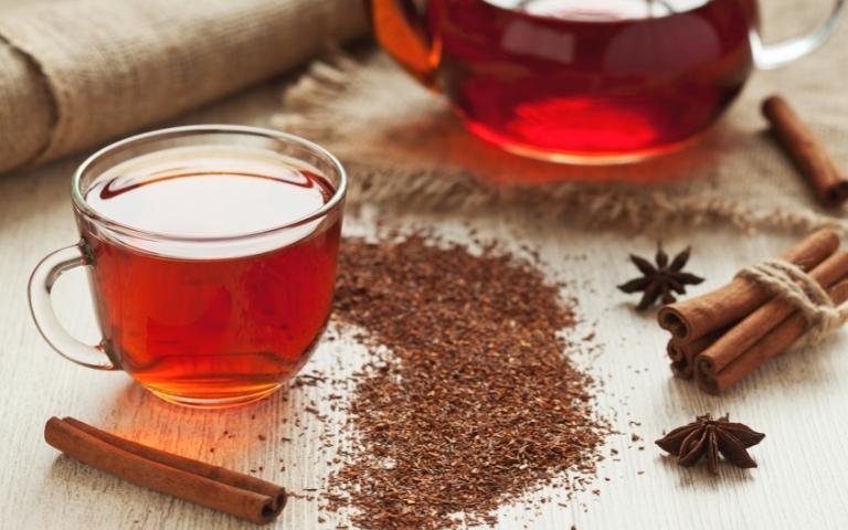 Rooibos tea infusion, with loose leaves scattered around and a bundle of cinnamon sticks.