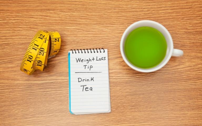 Notebook with "weight loss plan - drink tea" written on it and a cup of green tea.