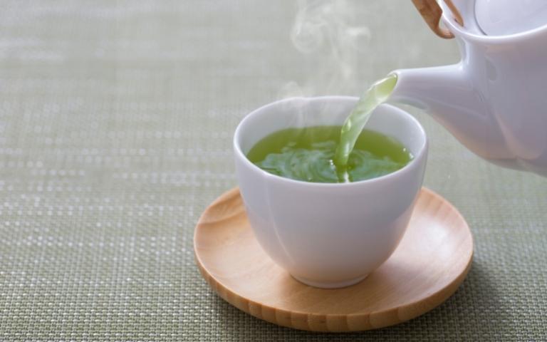 Pouring green tea from a teapot into a cup.