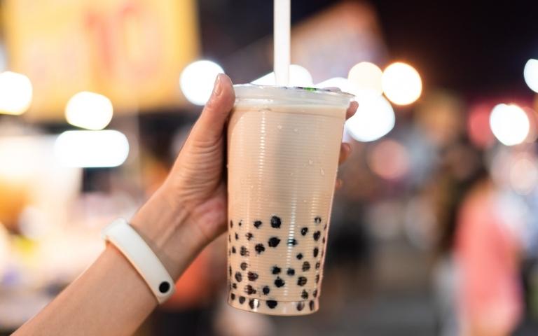 A hand holding a plastic cup with bubble tea and a plastic straw.