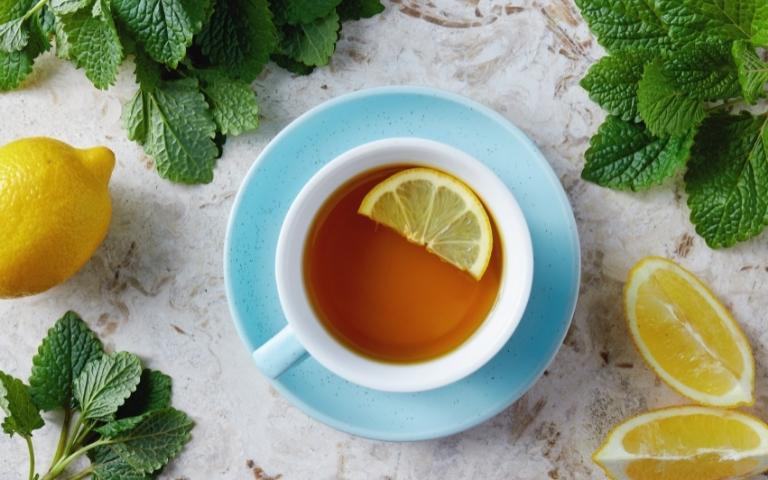 A cup of lemon balm tea surrounded by slices of lemon and lemon balm leaves.
