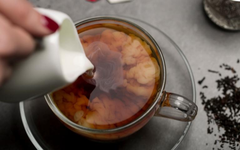 Pouring cream into a cup of black tea from a pitcher.