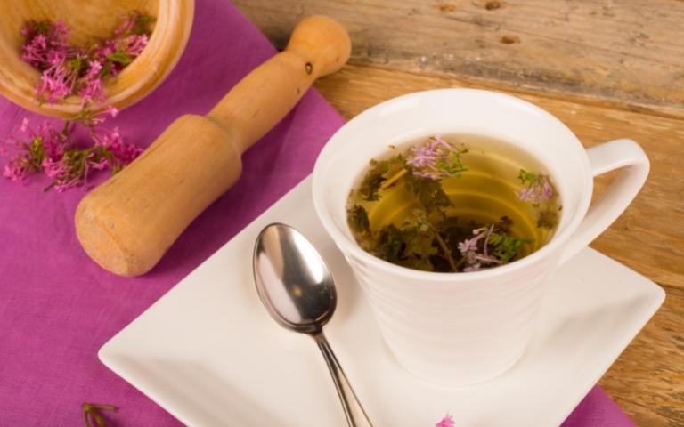 A cup of valerian tea near a bowl of ground fresh valerian.